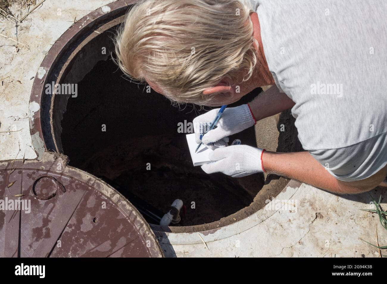 Der Mann beugte sich über den Wasserbrunnen und zeichnet die Messwerte des Wasserzählers auf. Überprüfung und Fixierung des Zählers. Stockfoto