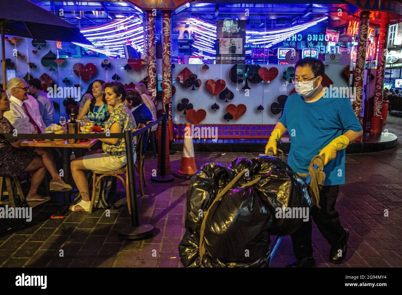 Leute, die auf Restauranttischen draußen essen und sauberer mit Gesichtsmaske und Handschuhen sind, tragen Müllsäcke in Soho, London, Großbritannien. Stockfoto