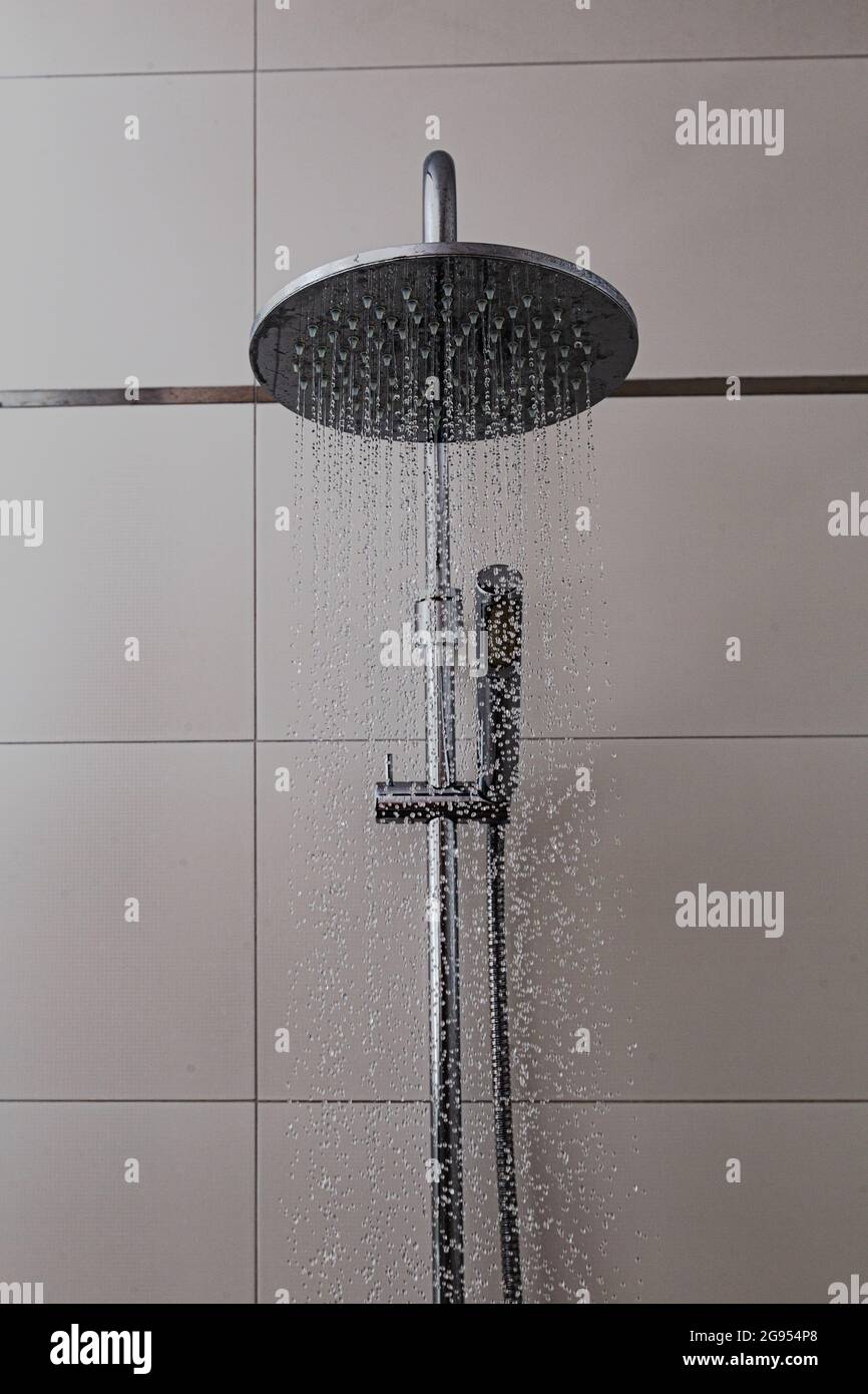 Dusche mit gefliestem Hintergrund im Badezimmer. Wasser fliegt in Tropfen aus Chrom-Duschen. Badausstattung als Ausstattungselement und modernes Design zu Hause. Stockfoto