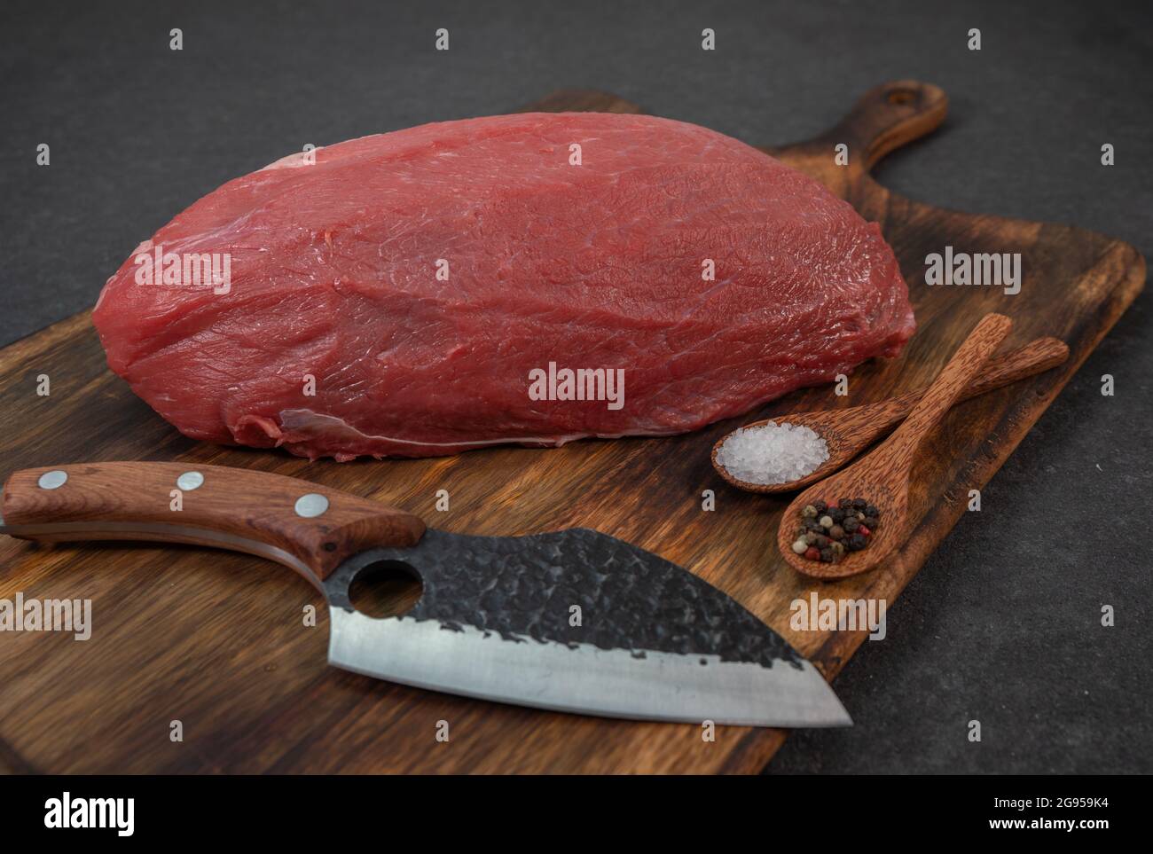 Nahaufnahme eines rohen Rinderfilets, auf einem hölzernen Schneidebrett mit Gewürzen und einem scharfen Messer Stockfoto