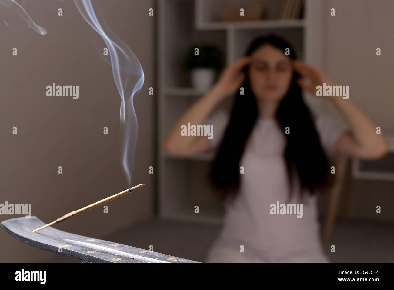 Ein aromatischer Indianerstab brennt, die Frau im Hintergrund meditiert. Aromatherapie, Selbsteintauchen, die Kraft des Denkens Stockfoto