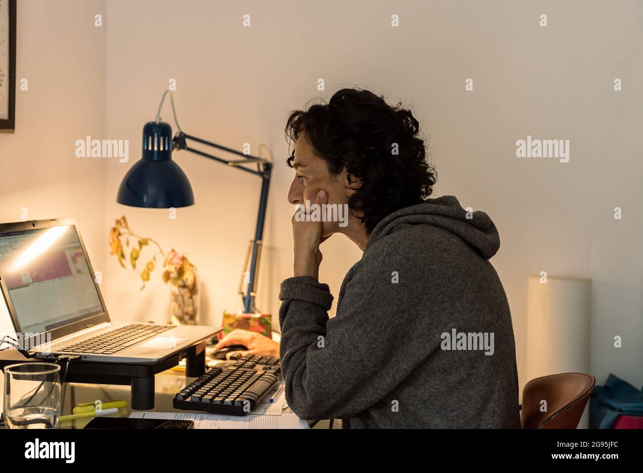 Junge Frau arbeitet online zu Hause mit Computer eine blaue Lampe auf Glastisch Stockfoto