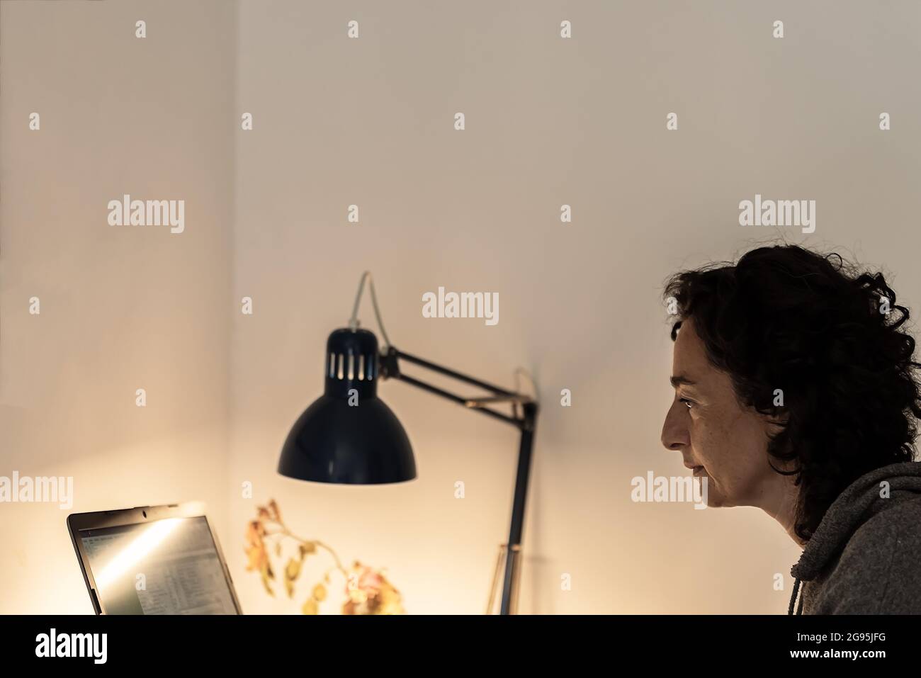 Junge Gesichtsfrau arbeitet online zu Hause mit Computer und blauer Lampe vor der weißen Wand Stockfoto