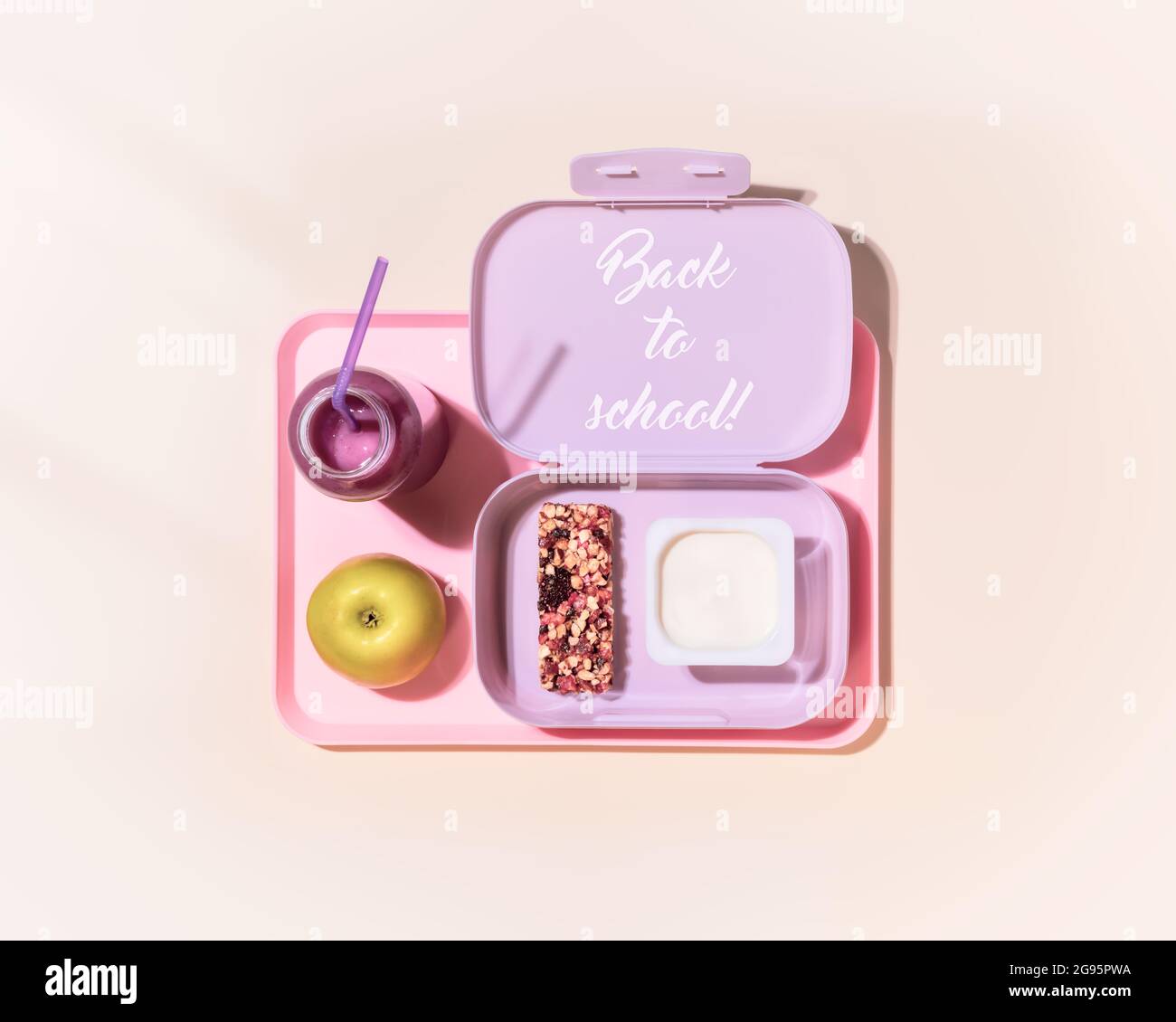 Zurück in den Schulurlaub. Zusammensetzung des Essens mit Lunchbox mit Joghurt, Müsliriegel, Apfel- und Beerencocktail auf rosa Hintergrund mit Inspiration zurück Stockfoto