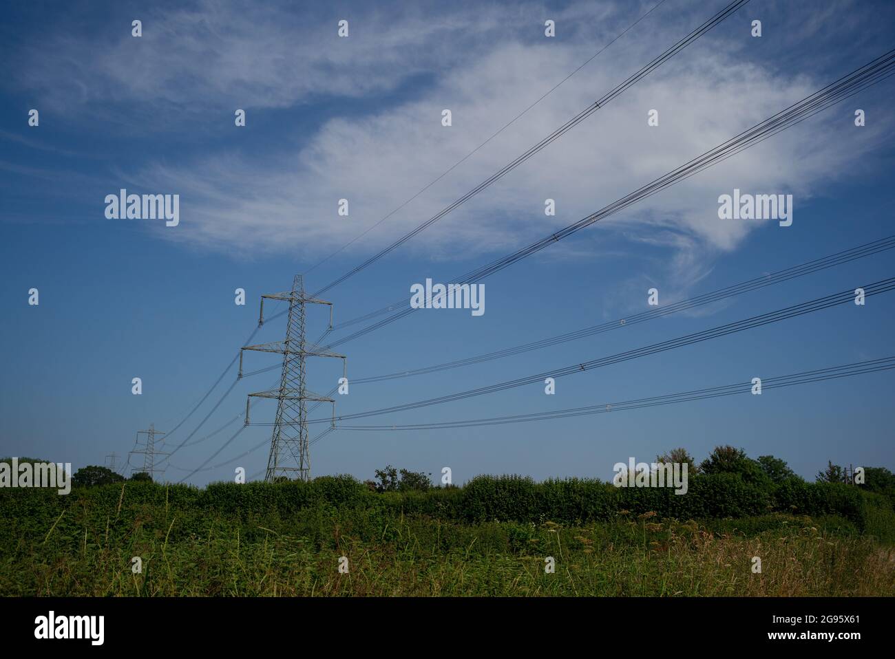 Eine Landschaftsansicht von Strommasten vor einem tiefblauen Sommerhimmel mit Wolken in einer ländlichen Umgebung mit Kopierraum. Stockfoto