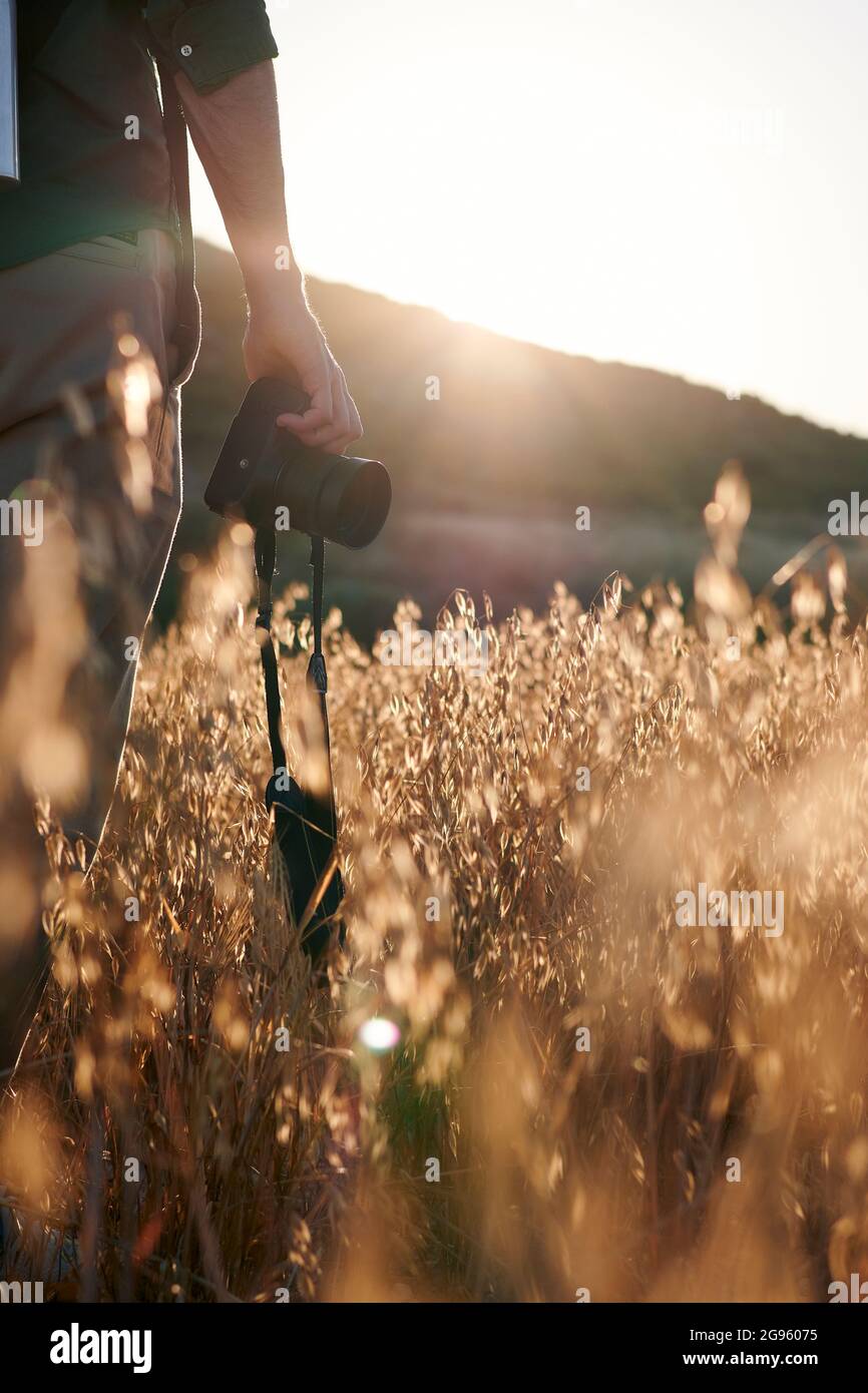 Nahaufnahme eines Fotografen, der bei Sonnenuntergang eine Kamera auf einer Wiese hält Stockfoto