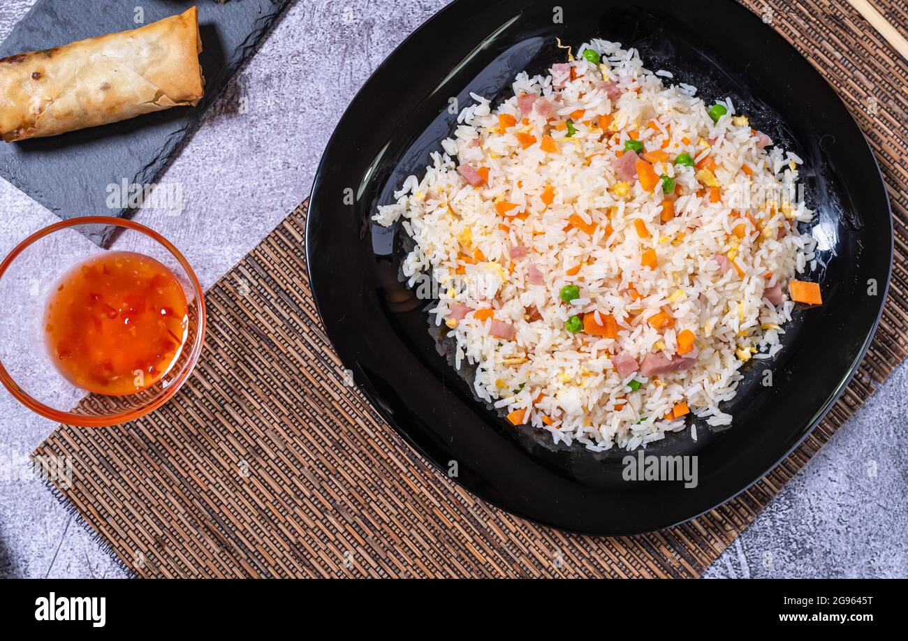 Blick von oben auf chinesisches Essen. Schwarzer Reisplatte 3 Köstlichkeiten, Schüssel mit süß-saurer Sauce und Frühlingsrollen. Asiatische Küche Stockfoto