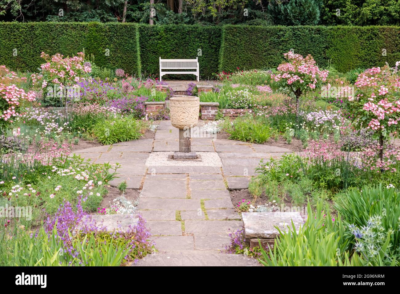 Ruhige Ecke eines gefackelten englischen formellen Gartens mit Blumenbeeten und einer Steinvase. Stockfoto