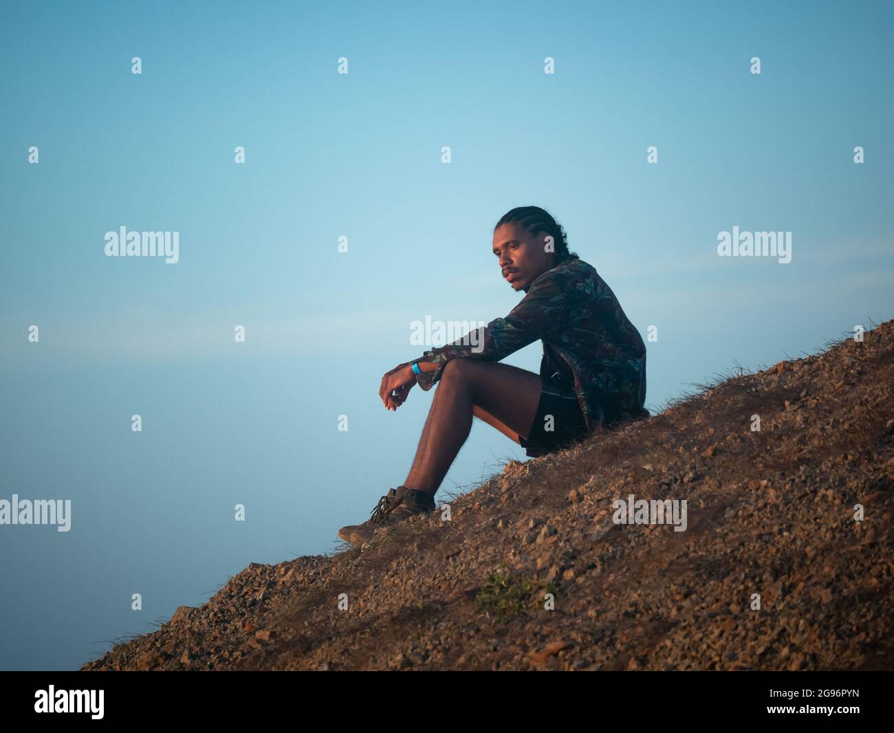 Uribia, La Guajira, Kolumbien - 28 2021. Mai: Junger brauner Lateinmann mit Zöpfen auf dem Kopf sitzt pensiv und wartet auf den Sonnenuntergang in der Wüste Stockfoto
