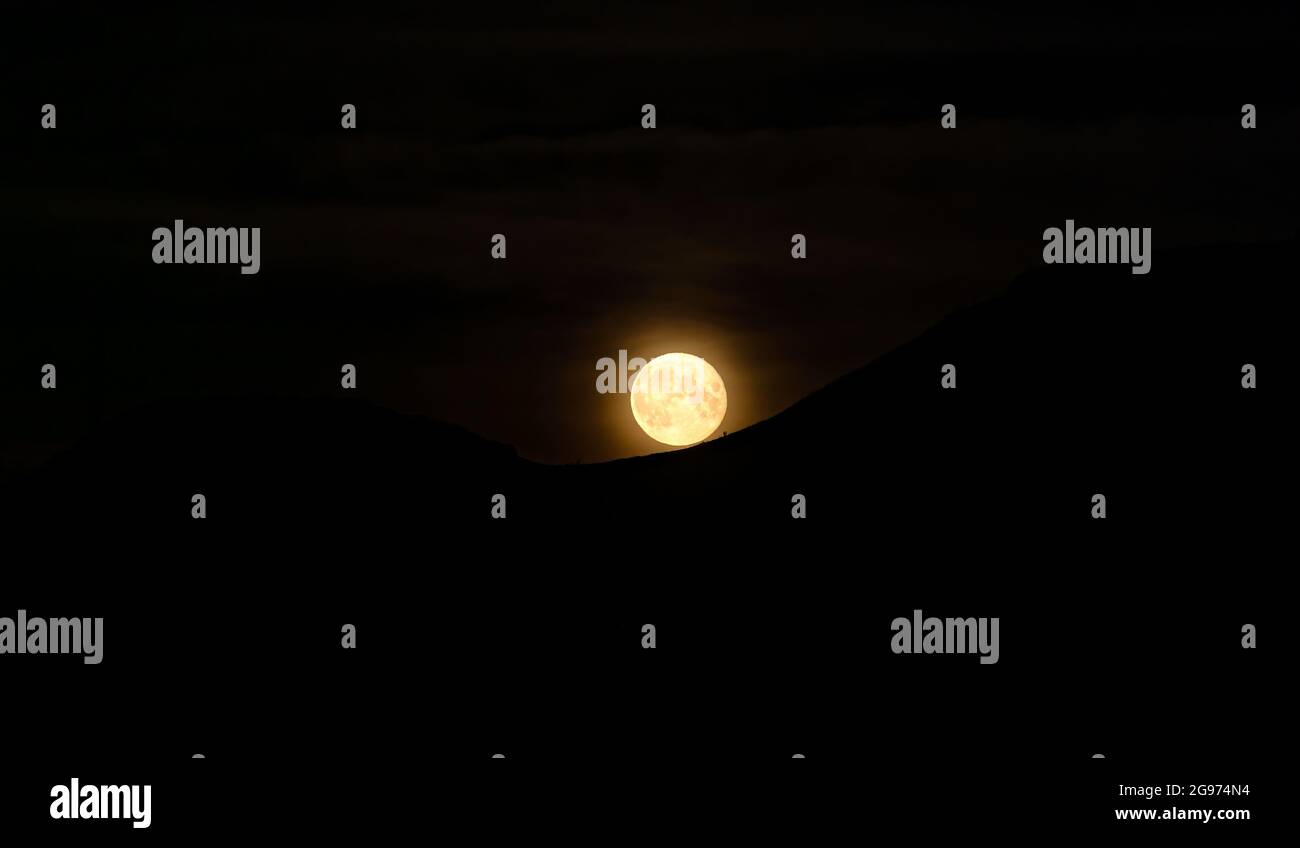 East Lothian, Schottland, Vereinigtes Königreich. UK Wetter: Juli 'Buck' Vollmond: Der Vollmond dieses Monats erscheint neben der Silhouette eines Bergrückens der Garleton Hills. Der Juli-Vollmond hat verschiedene Spitznamen, darunter Buck Moon, Raspberry Moon, Berry Moon, Salmon Moon oder Thunder Moon Stockfoto