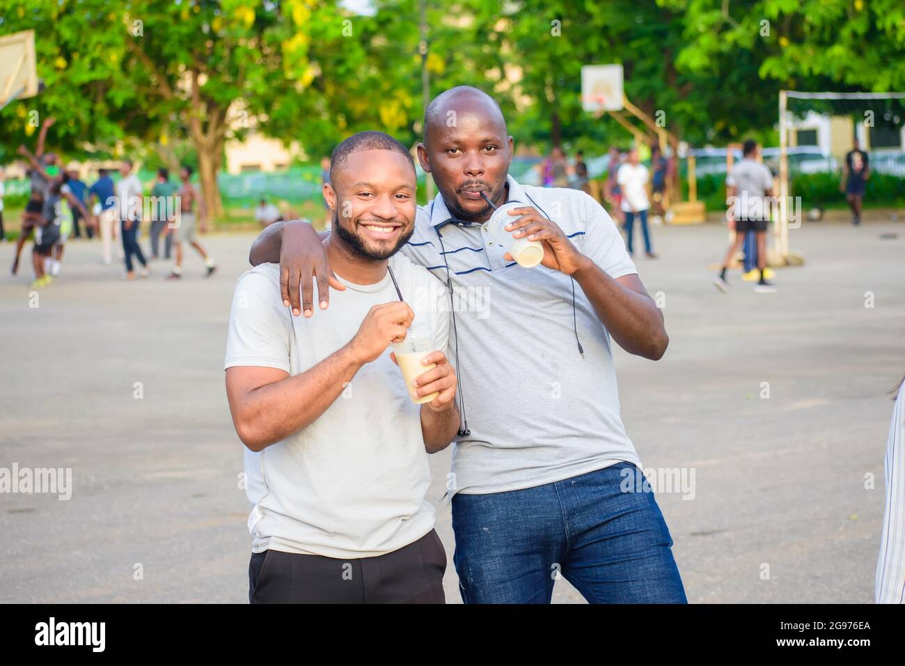 Zwei afrikanische Freundinnen stehen in ihrer Freizeit und trinken freudig Fruchtsaft in einem Freiluftpark Stockfoto