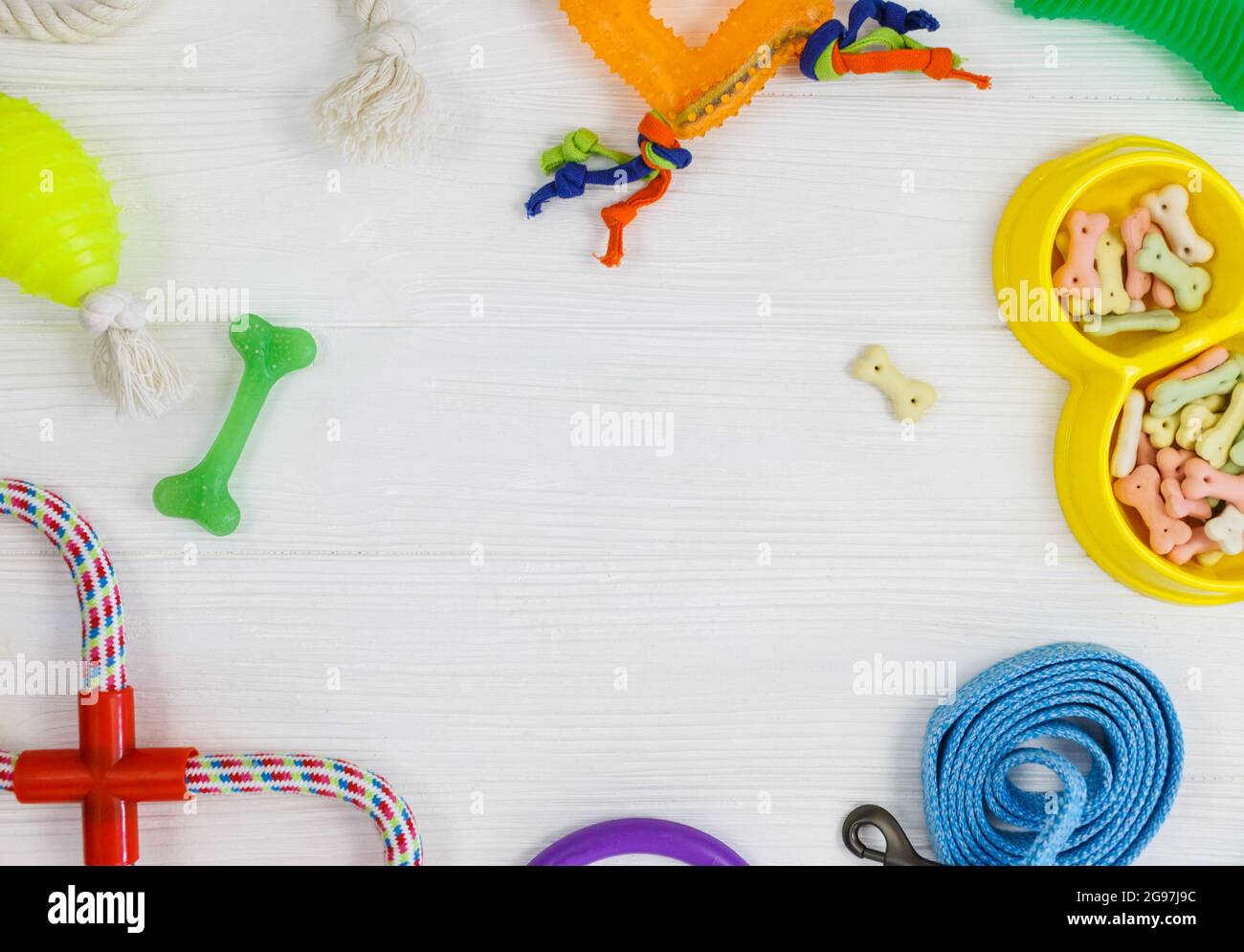 Gelbe Schale mit Snacks, Ball, Leine, ein Knochenspielzeug für Hunde auf weißem Holztisch. Set von Zubehör für Haustiere auf Holz. Nahaufnahme Stockfoto