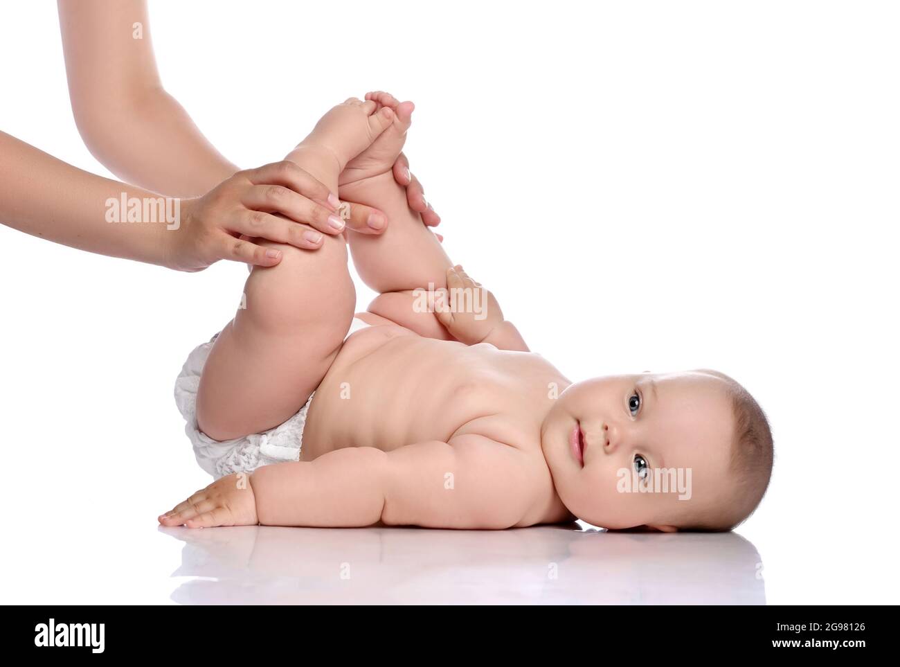 Happy infant Baby Mädchen Kind in Windel liegt auf ihrem Rücken macht Übungen, die Füße hoch mit erwachsenen Trainer halten. Seitenansicht Stockfoto