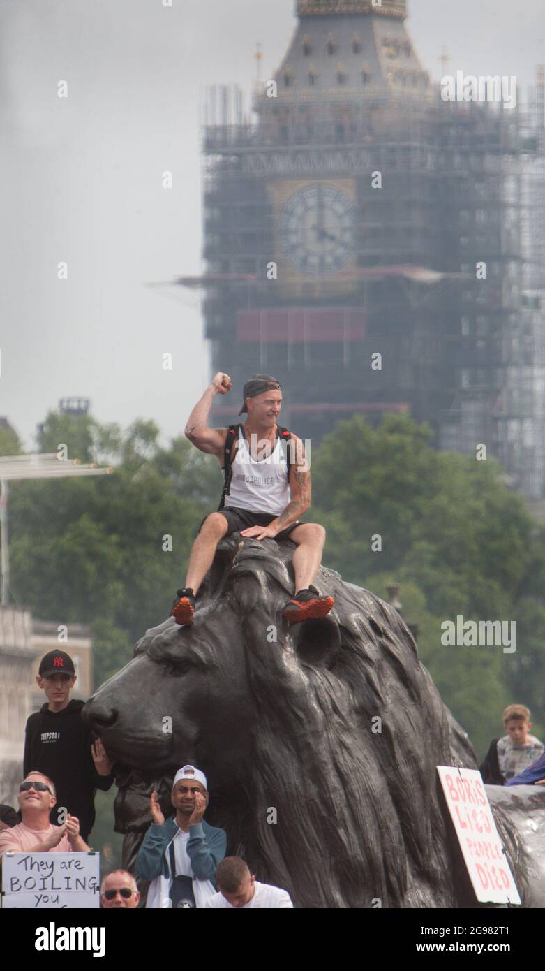 London, Großbritannien. Juli 2021. Ein Protestler reagiert positiv auf einen Redner mit einem erhabenen ersten, während er während der Demonstration auf einer Löwenstatue sitzt.Demonstranten protestieren im Rahmen der weltweiten Kundgebung für Freiheit am Trafalgar Square, London. Die Demonstranten demonstrieren gegen den Impfpass, die Covid-19-Impfung für Kinder und eine Reihe anderer Einschränkungen des Coronavirus. (Foto von Martin Pope/SOPA Images/Sipa USA) Quelle: SIPA USA/Alamy Live News Stockfoto