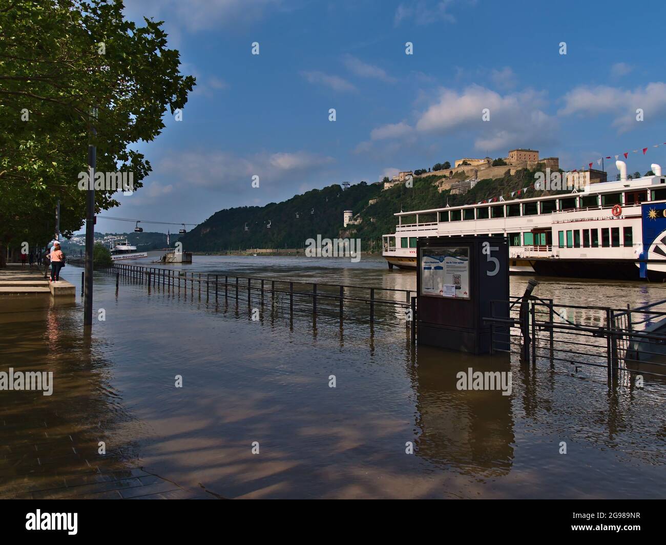 Menschen, die die überflutete Uferpromenade der Stadt Koblenz am Rheinufer mit hohem Wasserstand im Sommer und die Festung Ehrenbreitenstein betrachten. Stockfoto