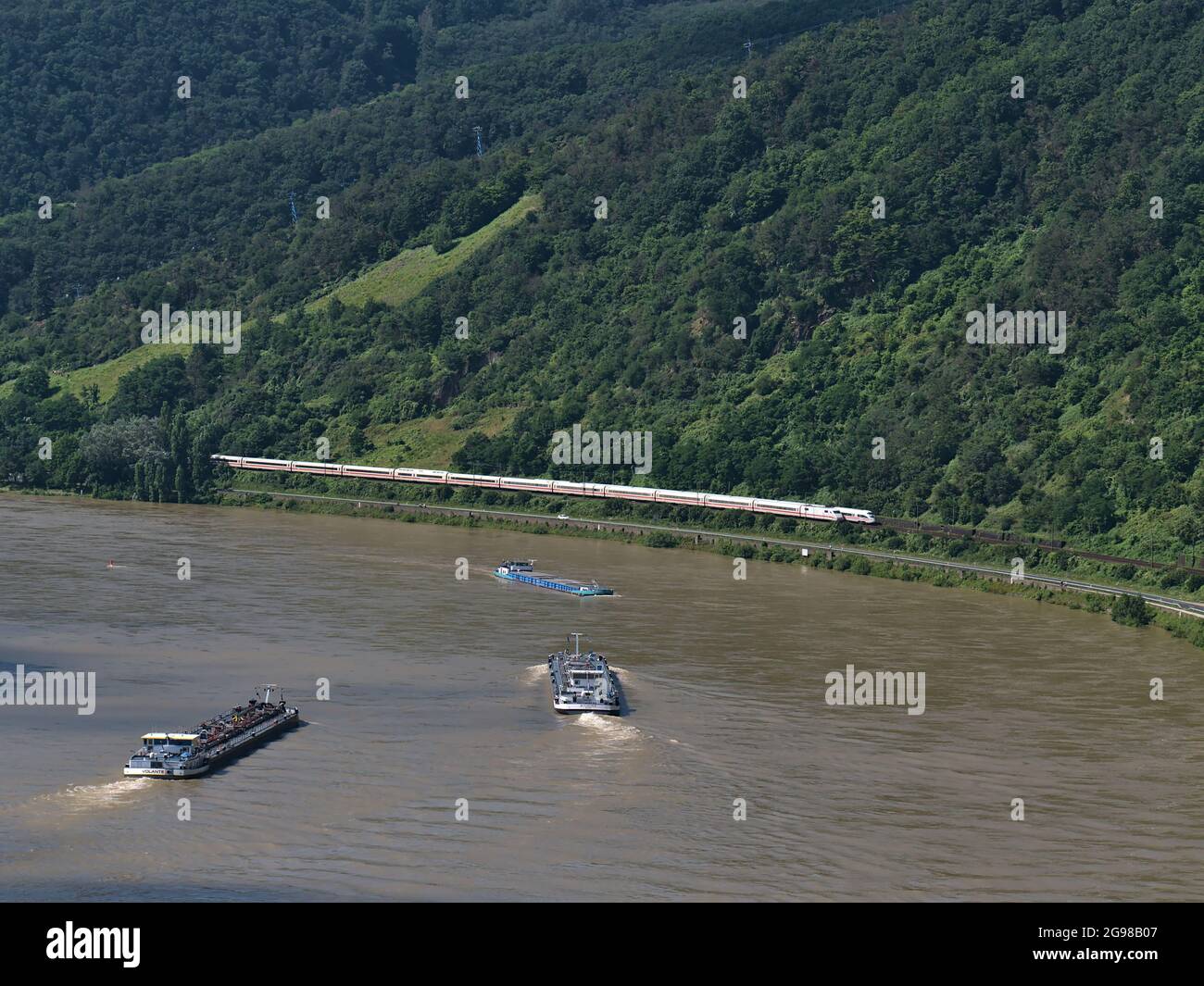 Luftaufnahme des Rheins, einer wichtigen Binnenschifffahrt, mit drei Frachtschiffen und zwei ICE-Zügen, die an sonnigen Tagen vorbeifahren. Stockfoto