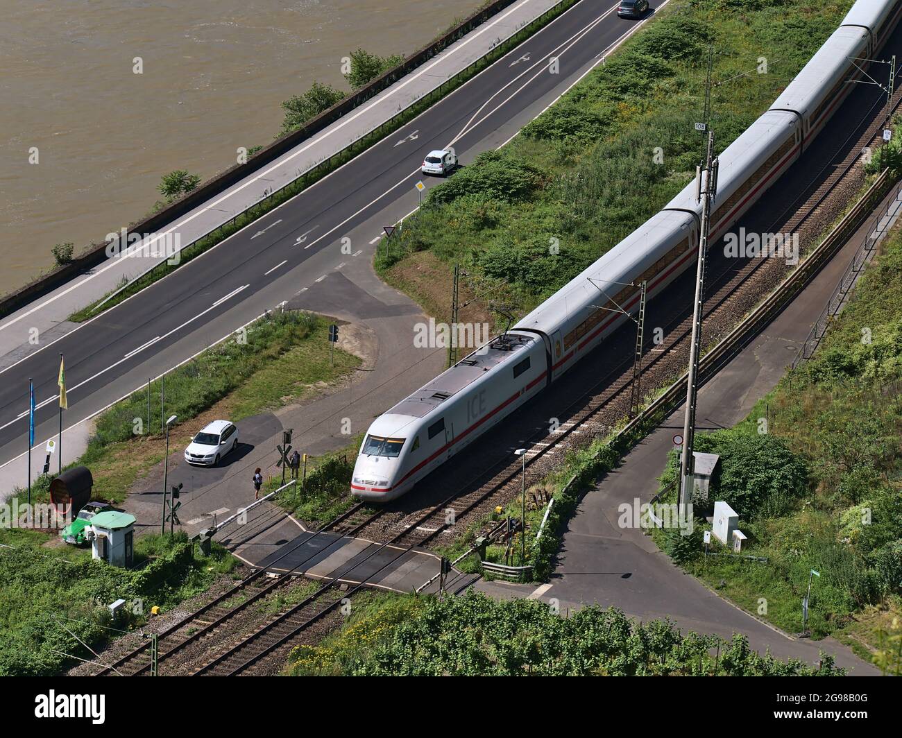 Luftaufnahme des InterCity Express (ICE) der Deutschen Bahn AG an einem Bahnübergang am Rheinufer mit Auto und Wartenden. Stockfoto