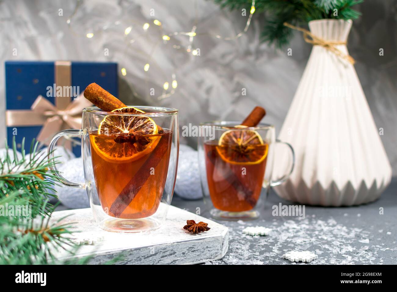 Warmer heiliger Wintertee in Glasküssen auf dem Hintergrund eines Kiefernzweiges. Weihnachtskarte. Zwei Tassen Tee mit Zitronen- und Zimtstangen schließen sich Stockfoto