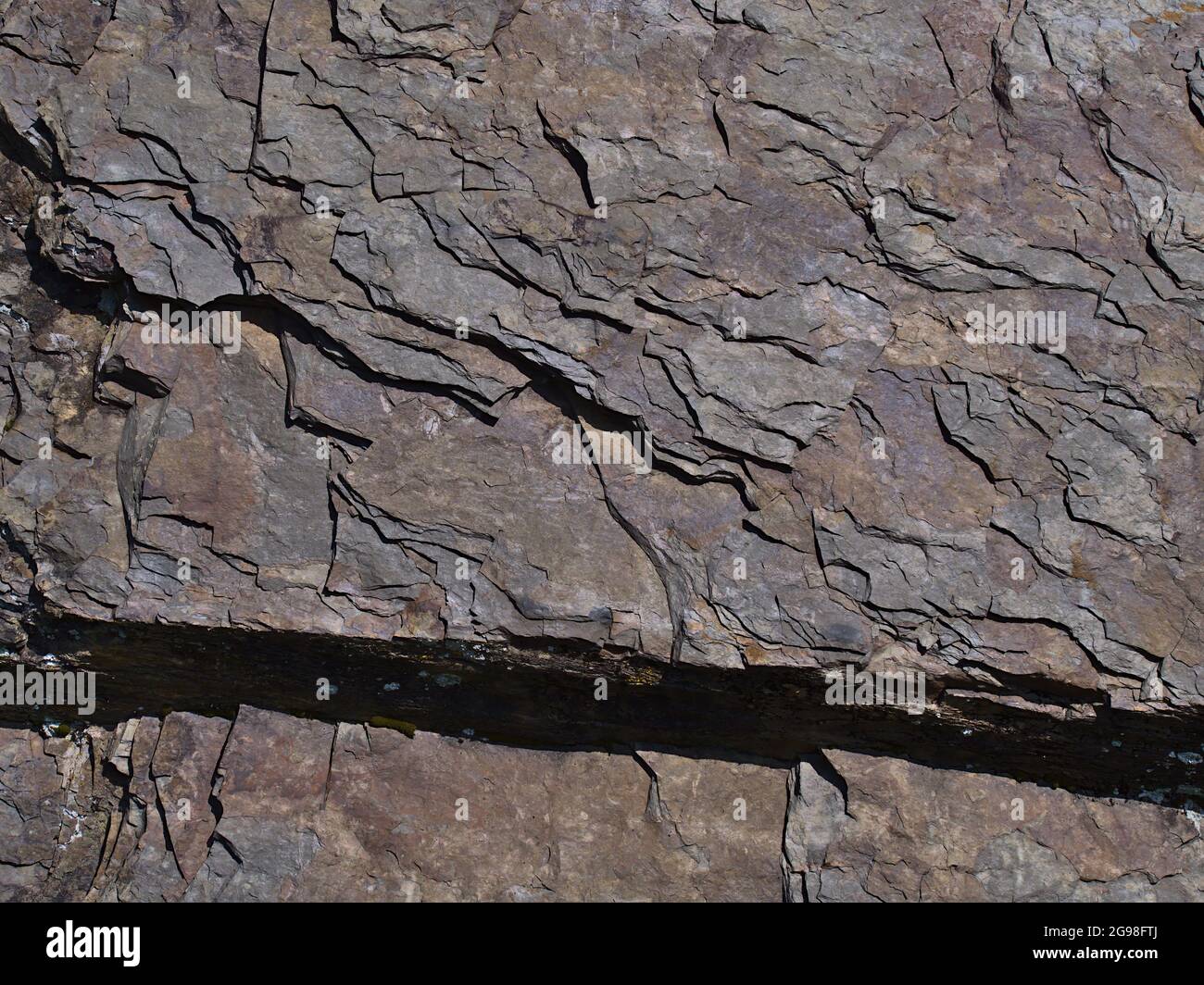 Nahaufnahme von Schiefer (auch Schiefer, Schiefer, ein metamorphes Gestein) mit sichtbaren rissigen Schichten und farbiger Oberfläche an sonnigen Tagen mit Schattenmuster. Stockfoto