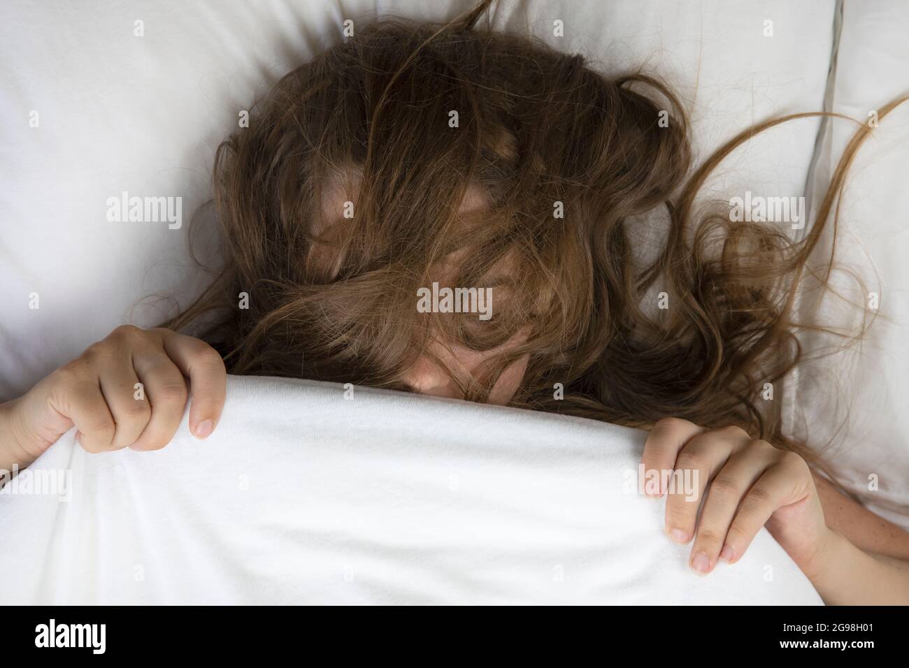 Schöne junge Frau, die im Bett mit unordentlichen braunen Haaren aus der Draufsicht schläft, mit weißen Bettlaken und Sommersprossen liegt Stockfoto