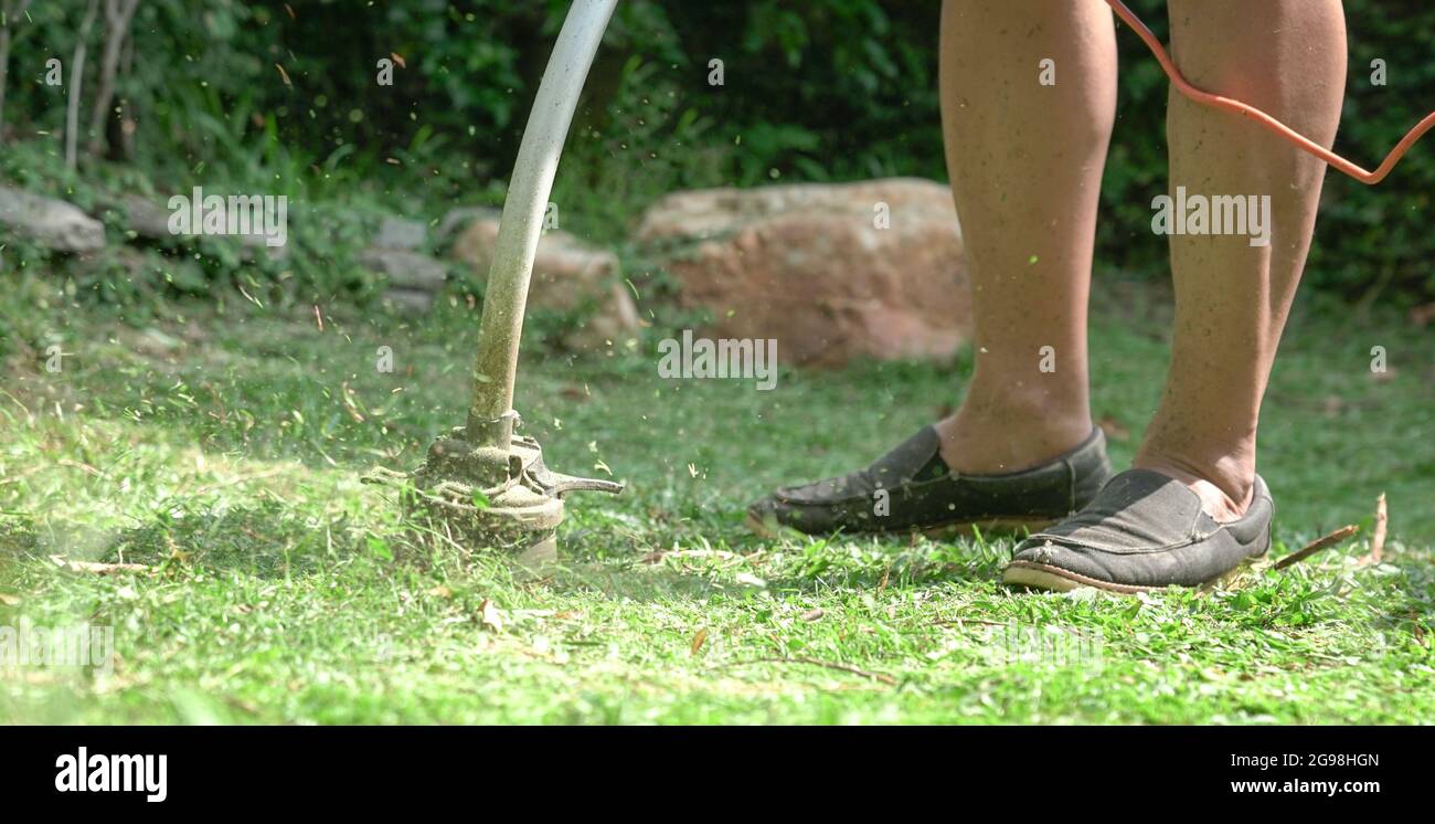 Mann mäht Rasen des Gartens mit elektrischen Rasentrimmer Maschine. Stockfoto