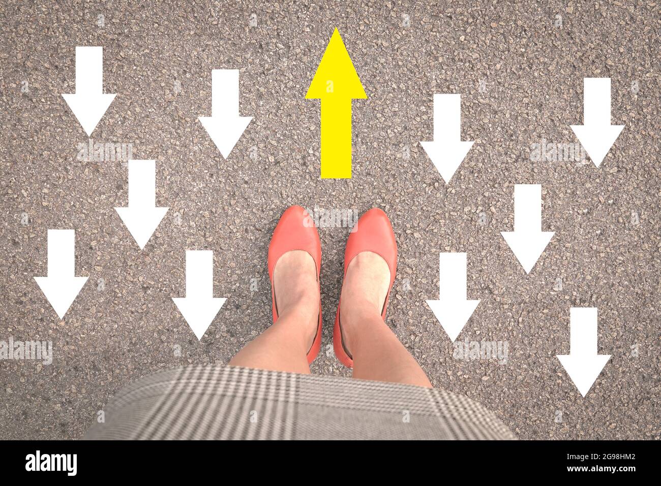 Geschäftsfrau, die mit orangefarbenen Schuhen auf der Straße steht, mit einem gelben Pfeil gegen die andere entgegengesetzte Richtung mit weißen Pfeilen. Stockfoto