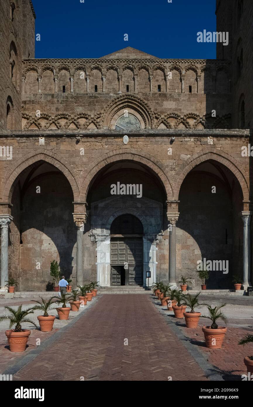 Über dem Portikus, den der Architekt Ambrogio da Como 1471 an der Westfront der römisch-katholischen Kathedrale Norman Duomo di Cefalù in Cefalu, Sizilien, hinzugefügt hat, erheben sich aus dem 12. Jahrhundert romanische blinde und verschachtelte Arkaden mit ausgeprägten Hundezahnverzierungen. Sie verbindet die zwei massiven normannischen Türme der Kathedrale und verfügt über drei Bögen, die äußeren zwei spitzen, die von vier Säulen und gerippten Gewölben unterstützt werden. Die Porta Regum (Königstür) unter dem Portikus ist ein fein dekoriertes Marmorportal, das von Fresken flankiert wird. Stockfoto