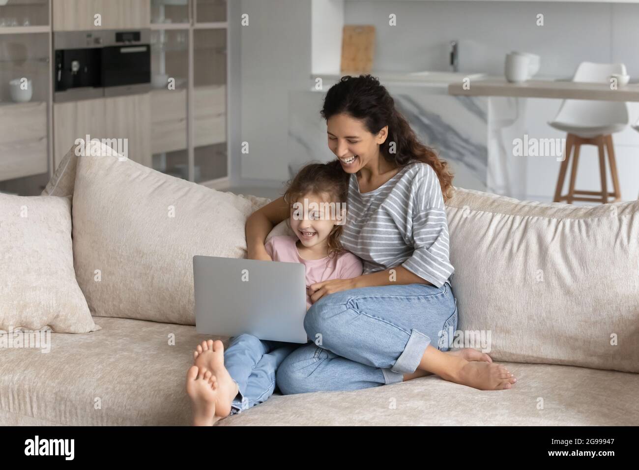 Lächelnde lateinische Mutter und Tochter verwenden zu Hause einen Laptop Stockfoto