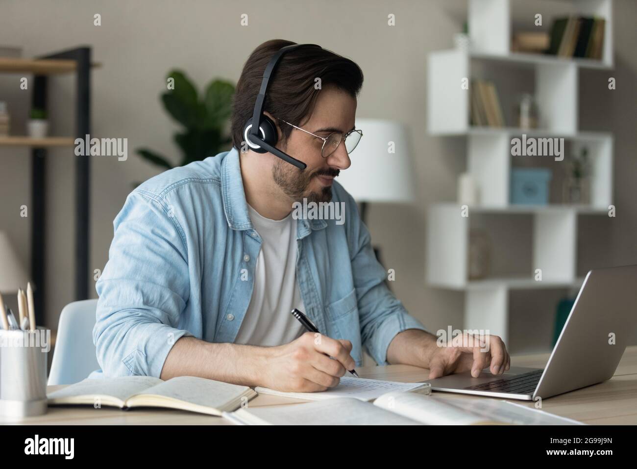 Mann trägt Headset hört Audio-Kurs macht Notizen Lernen online Stockfoto