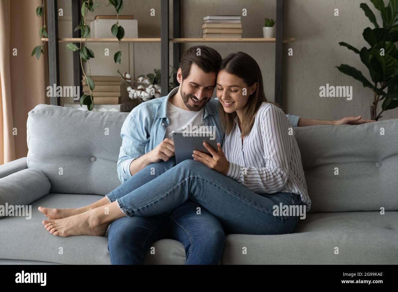 Verliebte Paare sitzen auf dem Sofa mit einem modernen Tablet-Gerät Stockfoto