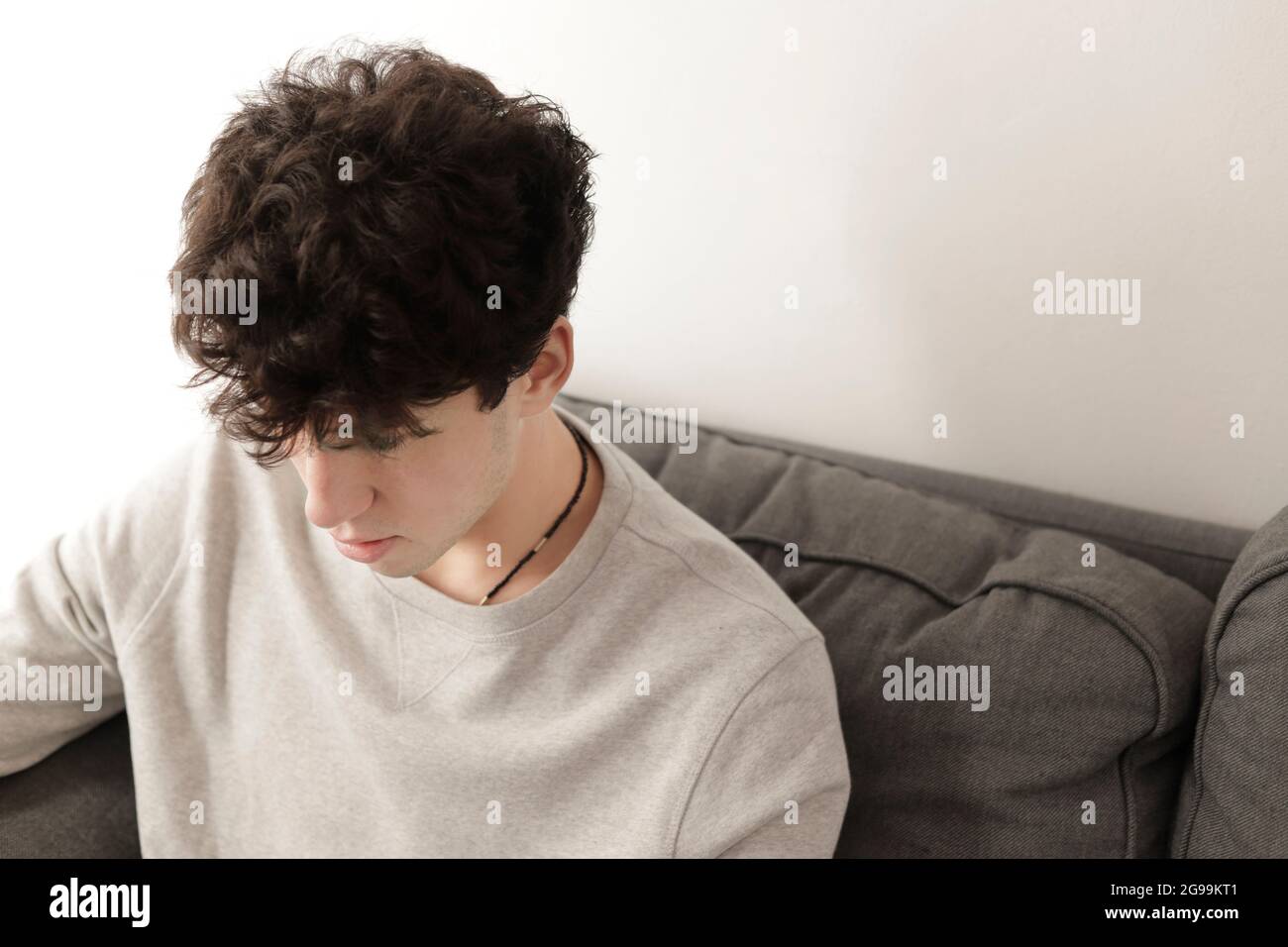Junger Mann mit reichlich Haaren, der auf ein Sofa schaut. Lockiger Kerl Stockfoto
