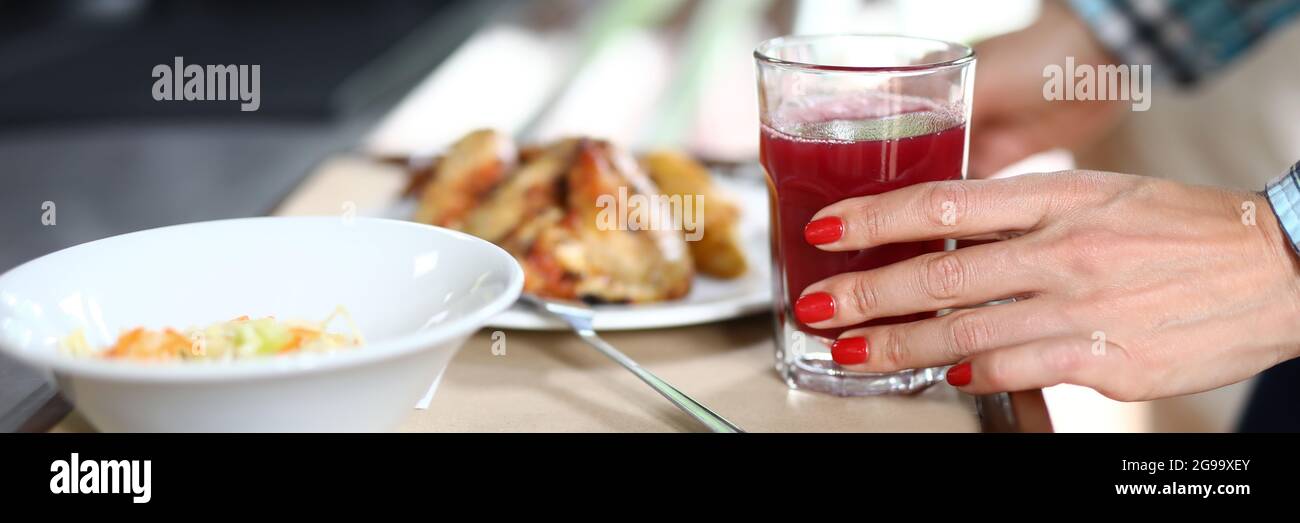 Auf dem Tablett sind Teller mit Essgeschirr, weibliche Hand hält Glas rote Flüssigkeit Stockfoto