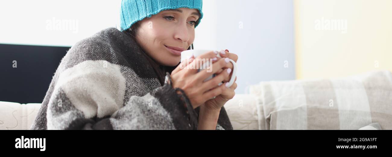 Gekühlte Frau auf der Couch in Decke und Hut hält heiß becher Stockfoto Gekühlte Frau auf der Couch in Decke und Hut hält heiß becher Stockfoto
