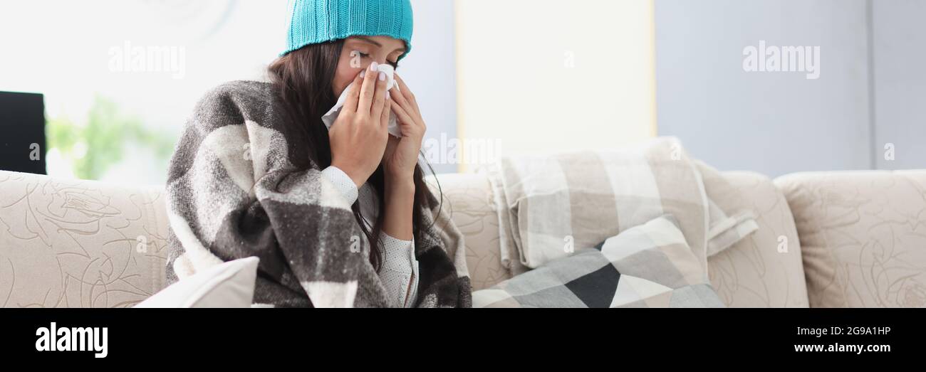 Gekühlte Frau auf Sofa in Decke und Hut hält Taschentuch Stockfoto Gekühlte Frau auf Sofa in Decke und Hut hält Taschentuch Stockfoto