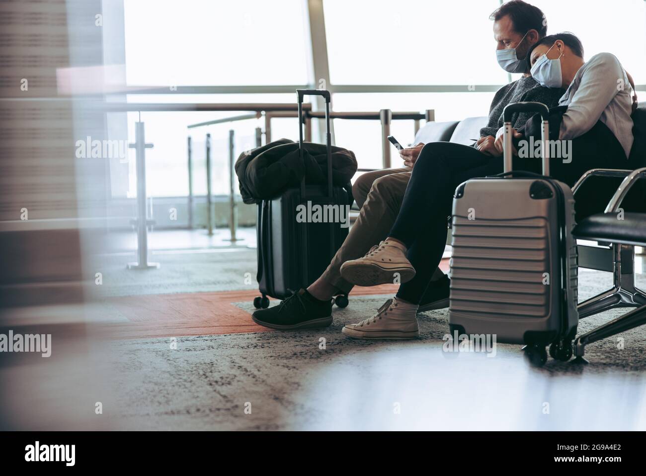 Ein paar Reisende mit Gesichtsmasken sitzen in der Bordlounge des Flughafens. Mann und Frau warten auf verspäteten Flug am Flughafen. Stockfoto