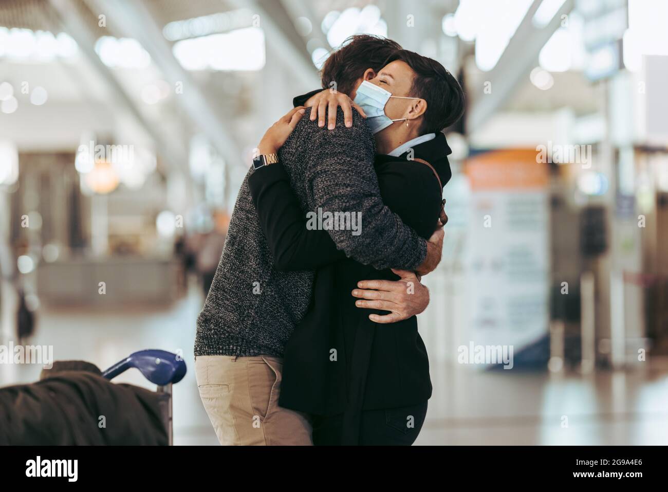 Frau begrüßt Mann am Flughafen nach Pandemie. Separates Treffen des Paares am Flughafen nach der Aussperrung der Pandemie. Stockfoto