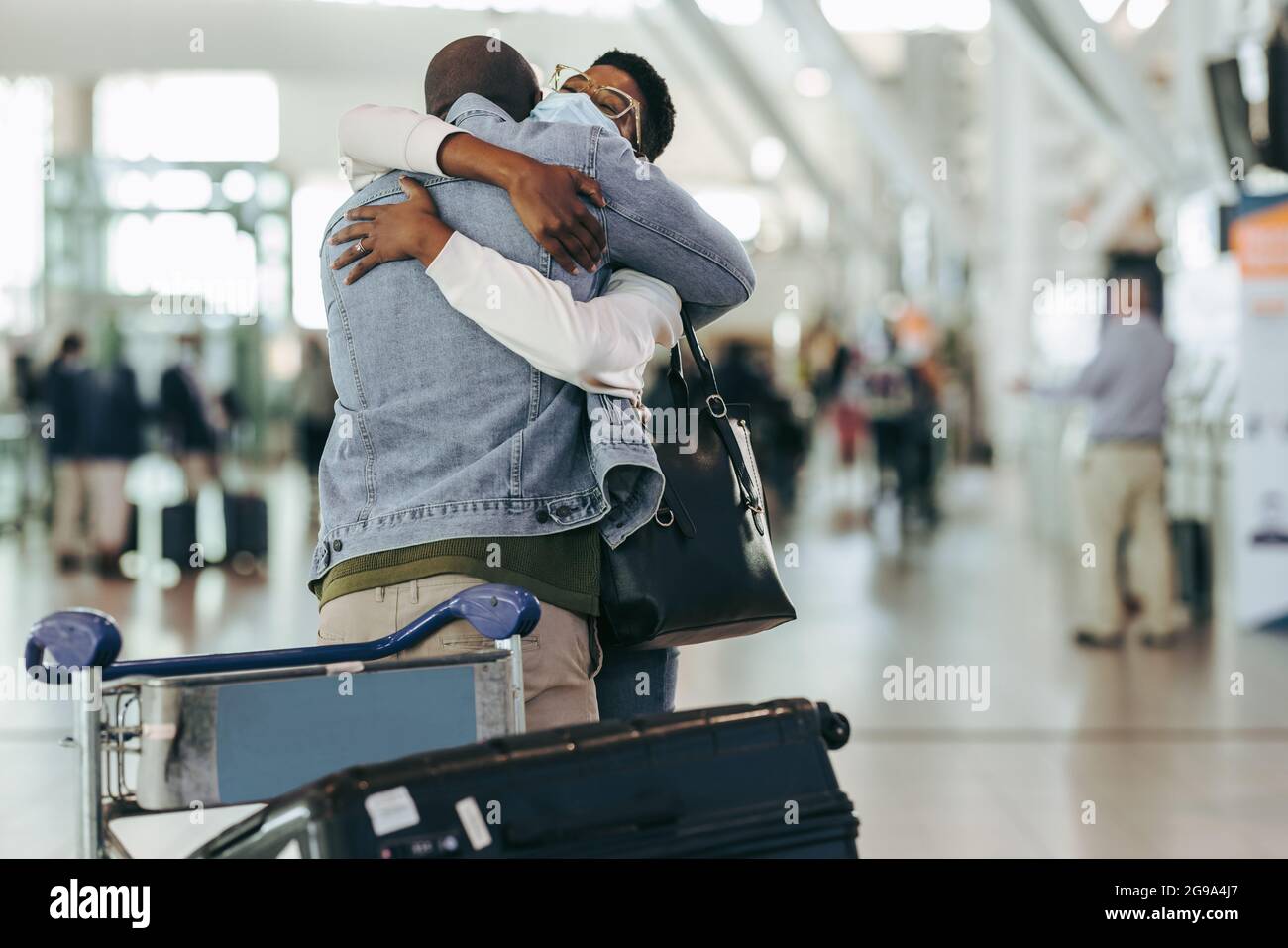 Afrikanisches Paar traf sich nach der Trennung wegen Covid am Flughafen. Mann und Frau umarmen sich am Ankunftseingang des Flughafenterminals. Stockfoto
