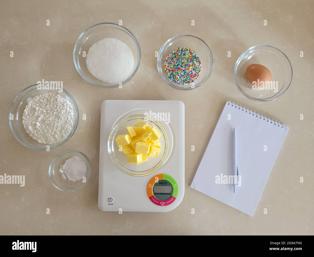 6 Schüssel mit Zutaten, Schüssel auf digitaler Küchenwaage, Notizblock und Stift Stockfoto