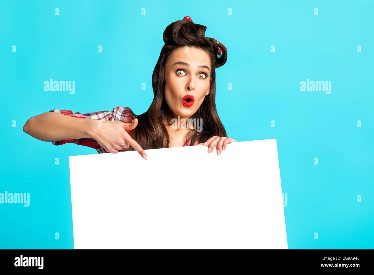 Schockierte Pinup Dame zeigt auf leere Banner auf blauem Studio-Hintergrund, Mockup für Anzeige, Promo, Verkauf Stockfoto