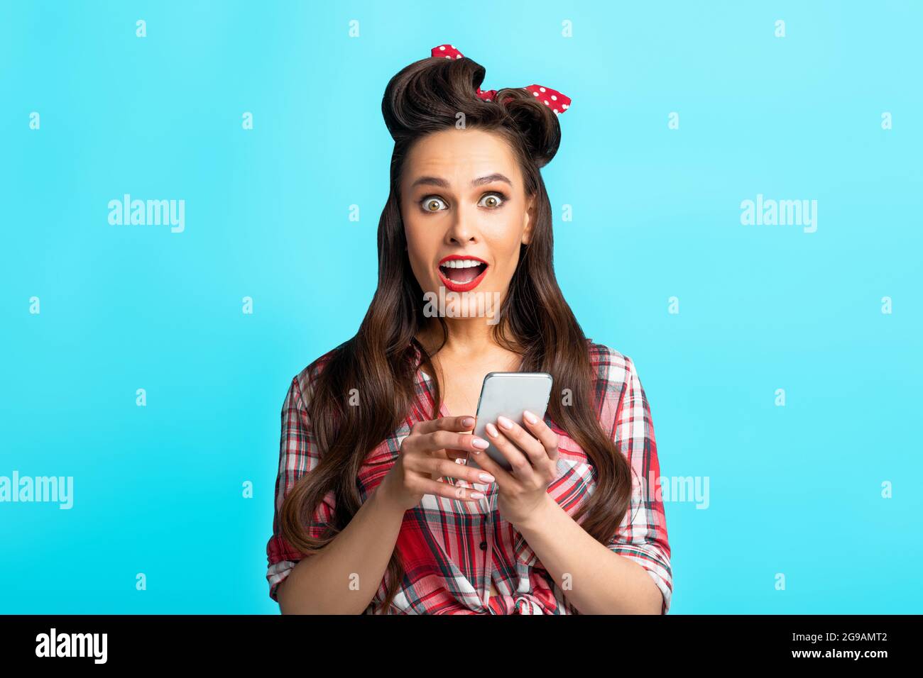 Aufgeregt junge Pinup Frau im Retro-Outfit mit Smartphone über blauen Studio-Hintergrund Stockfoto