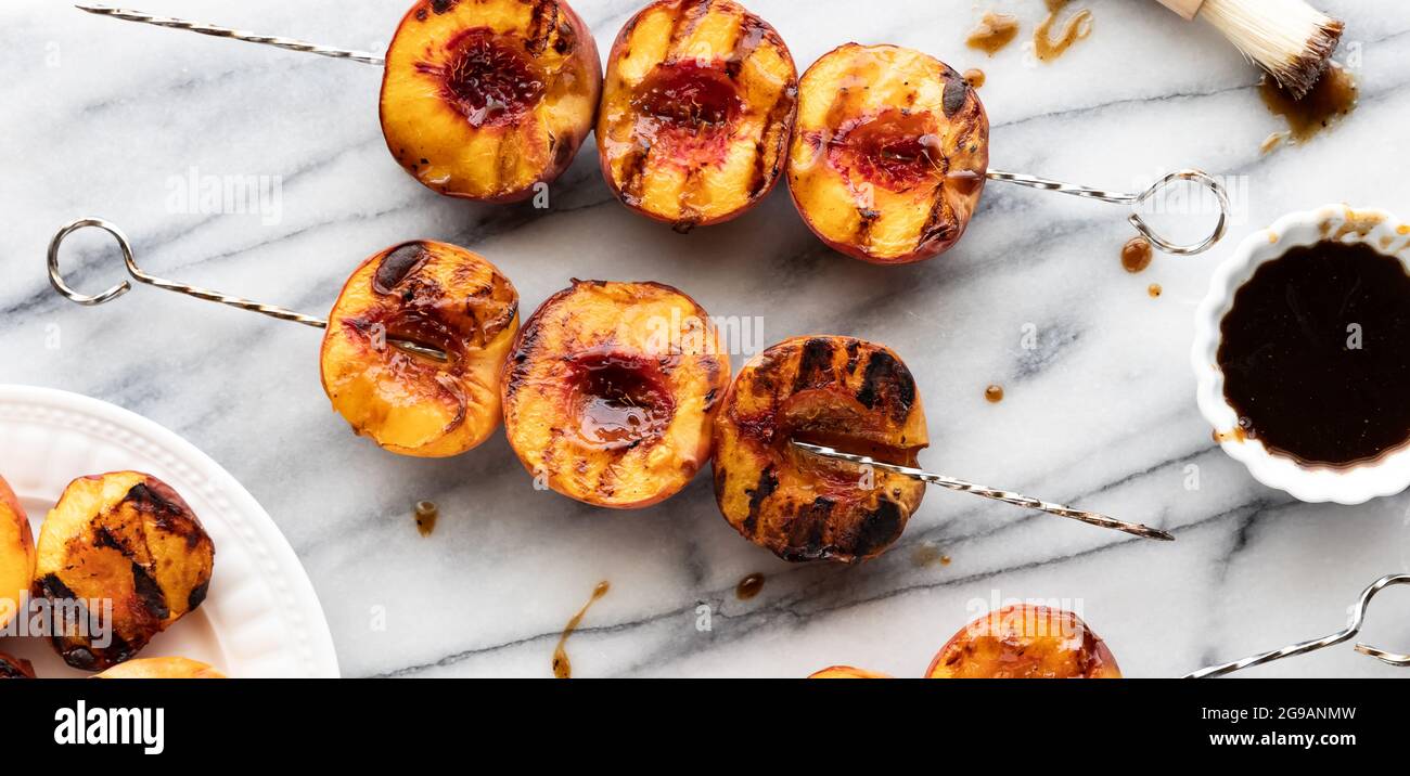 Blick von oben auf gegrillte Pfirsichspieße auf einem Marmorklatsch mit süßer Barbecue-Sauce. Stockfoto