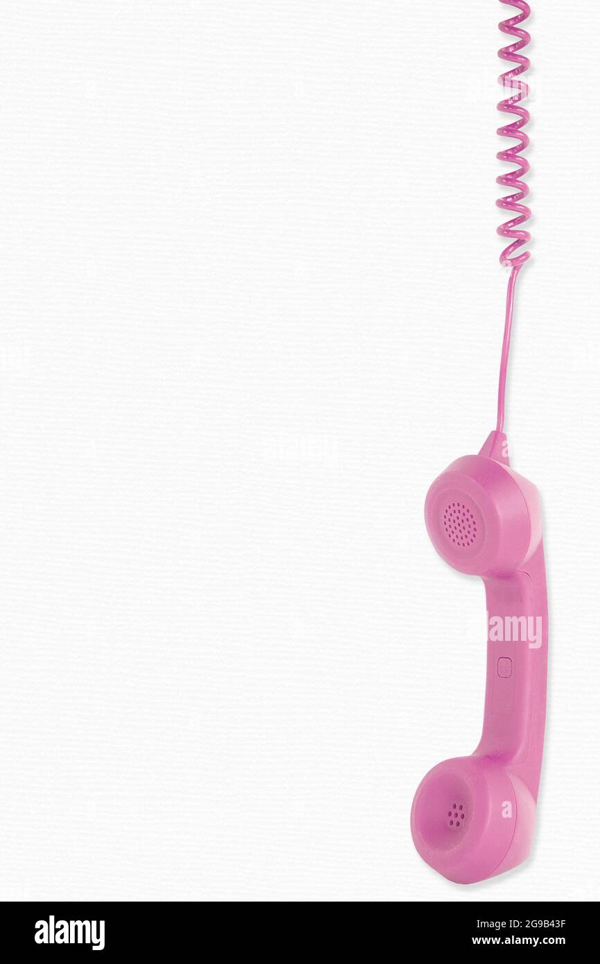 Rosafarbener Telefonempfänger, der am Telefonkabel auf weißem Hintergrund baumelt Stockfoto