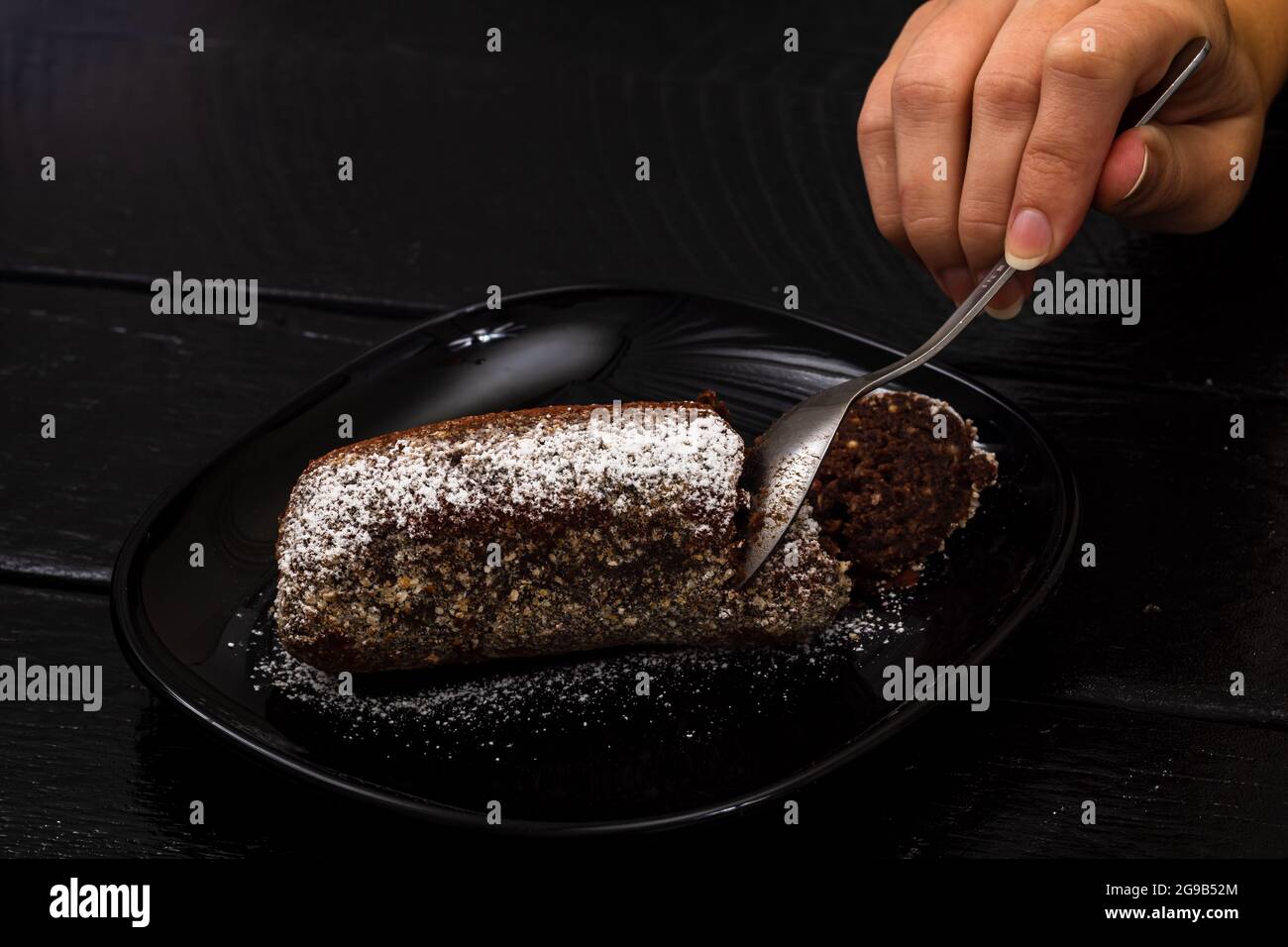 Eine Nahaufnahme der weiblichen Hand, die ein Stück aus einem Schokoladenmousse-Kuchen nimmt Stockfoto