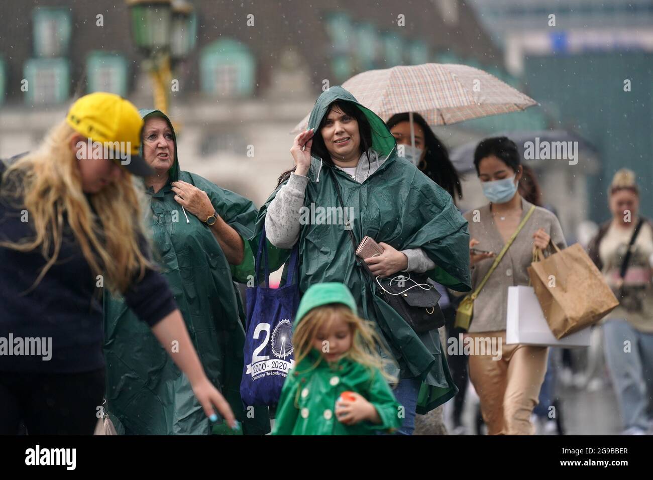 Eine Gruppe von Menschen geht über die Westminster Bridge, während starker Regen durch das Zentrum Londons fegt. Gewitter, die Blitze und sintflutartige Regenfälle in den Süden bringen, werden bis Montag anhalten, sagten Prognostiker. Bilddatum: Sonntag, 25. Juli 2021. Stockfoto