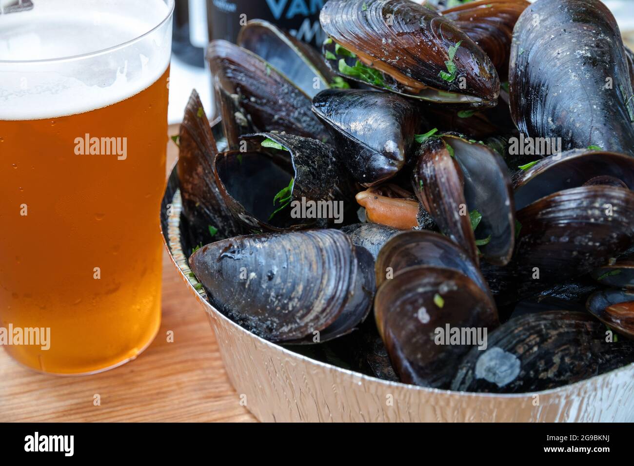 Frische, gekochte Muscheln mit Petersilie in eine silberne Schüssel und ein kaltes Bier in ein Glas. Fest der Bier und frischen Fisch und Meeresfrüchte. Gedünsteter Glas mit kaltem Bier auf den Tisch. Stockfoto