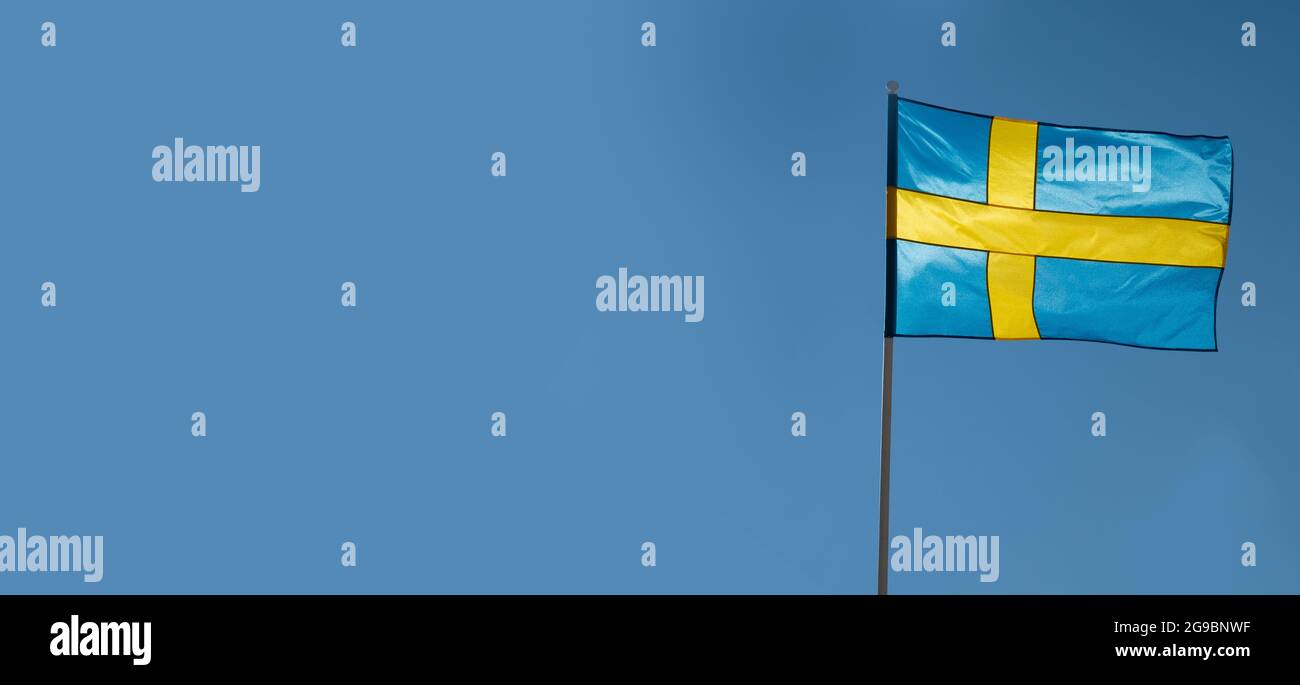 Flagge Schwedens auf blauem Himmel Hintergrund. Leerer Kopierbereich für Text. Schwedische Flagge winkt bei Wind und Sonnenlicht Stockfoto