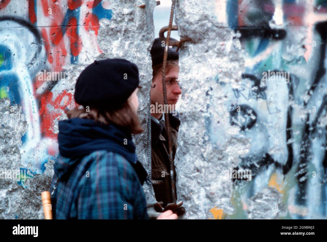 Ein westdeutsches Mädchen spricht mit einer ostdeutschen Garde durch eine Öffnung in der Berliner Mauer, circa 1980er Jahre Stockfoto