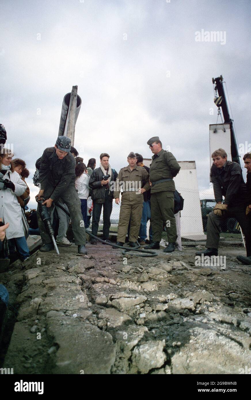 Die DDR-Polizei und westdeutsche Bürger beobachten, wie ein Arbeiter einen Teil der Berliner Mauer am Potsdamer Platz, 1989, demontierte Stockfoto