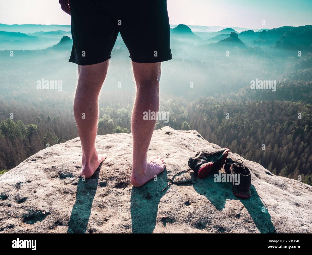 Barfuß schlanke Beine mit haarigen Kälbern eines männlichen Läufers, der  neben abgenommenen verschwitzten Laufschuhen an einem felsigen Rand über  einem langen tiefen vally in der Natu steht Stockfotografie - Alamy