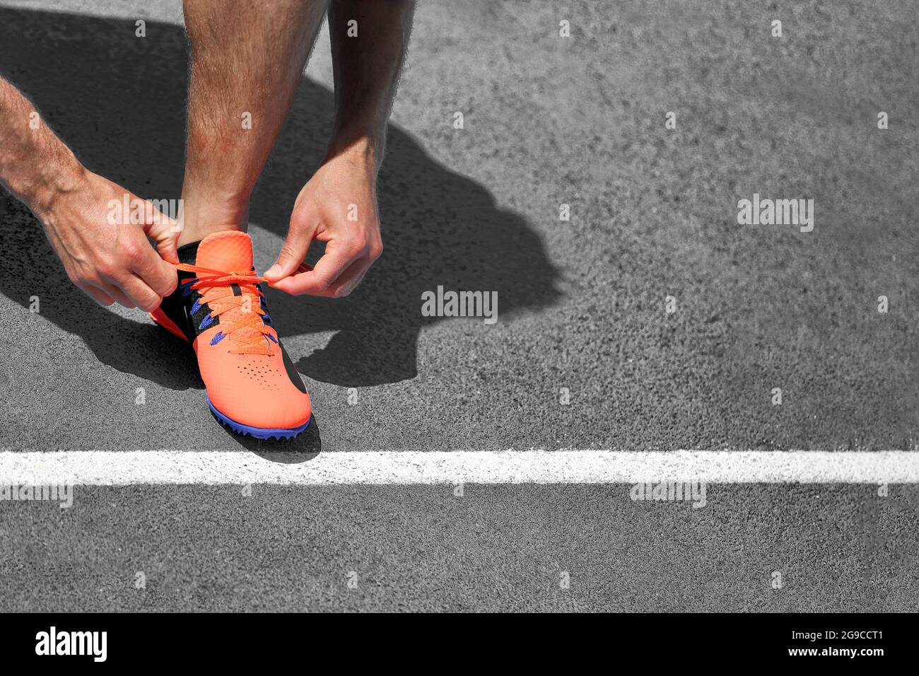 Läufer Mann bereit, auf Asphalt Straße laufen zu beginnen binden Laufschuhe Schnürsenkel auf grauem Hintergrund. Platz für Text mit Startzeile kopieren. Stockfoto